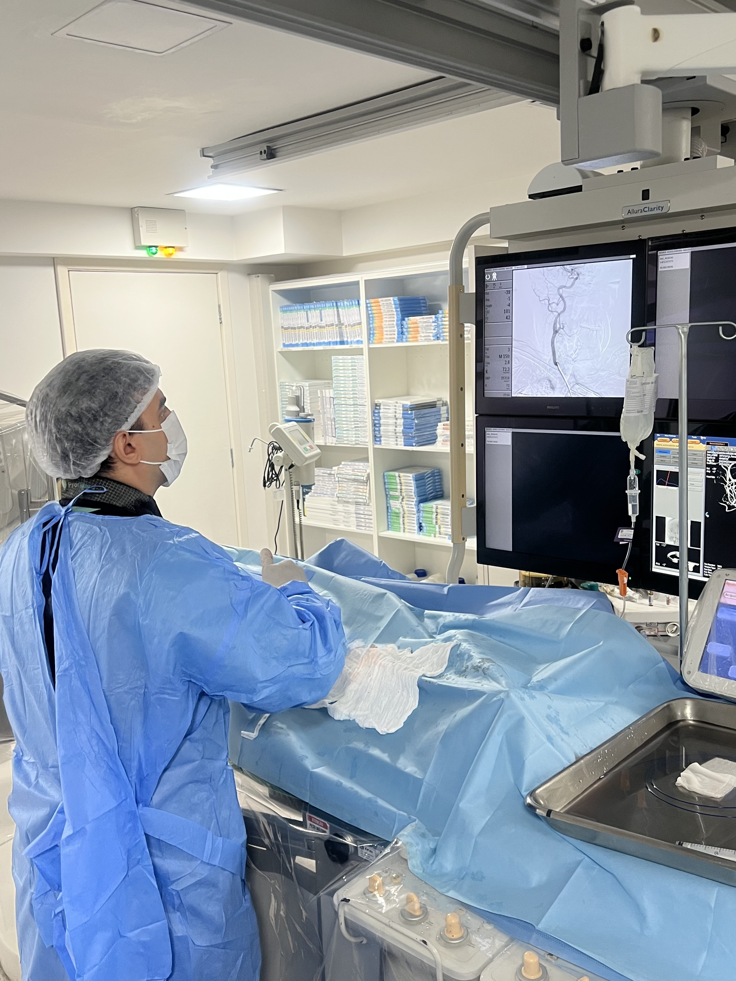 Dr. Matheus Costa em sala de hemodinâmica analisando imagens de angiografia cerebral durante procedimento endovascular